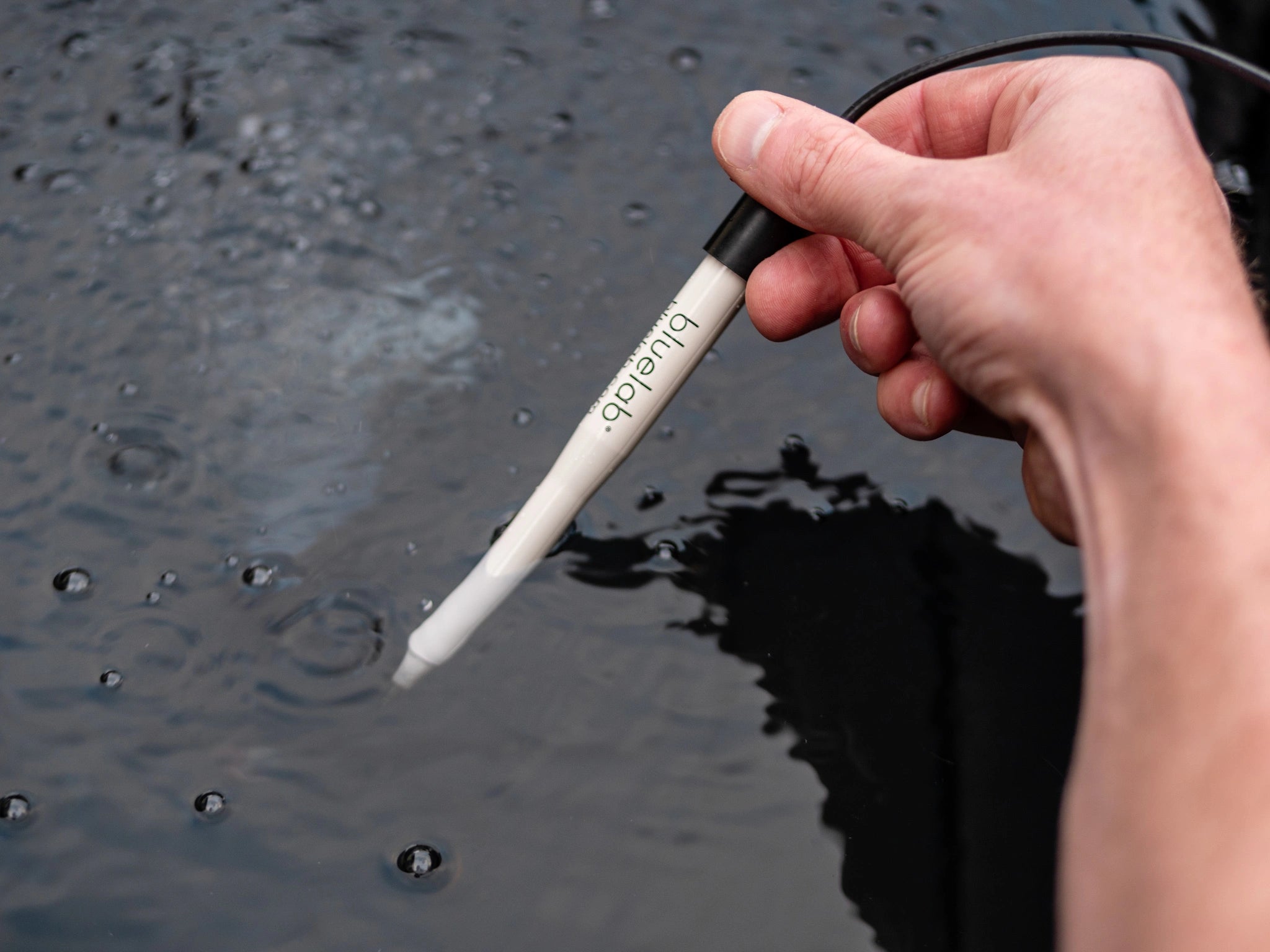 Hand holding a pH test pen over water with bubbles, brand 'Bluelab' visible.